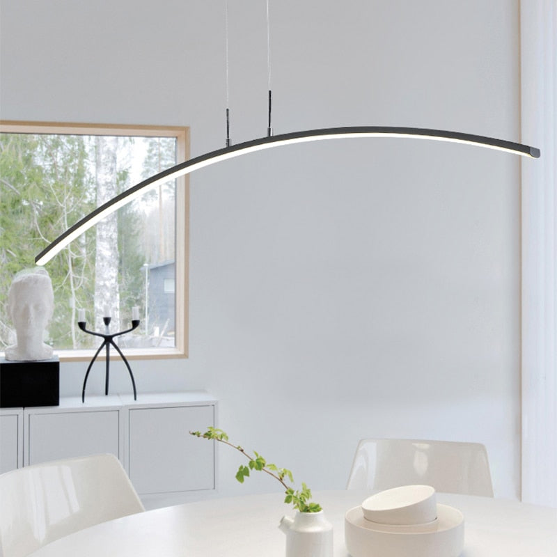 Curved Modern LED pendant light with a minimalism design, installed over a dining table in a bright interior setting.